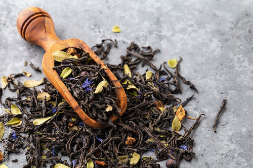 Dry black tea mixed with herbs, flower petals and berries on gray background. photo