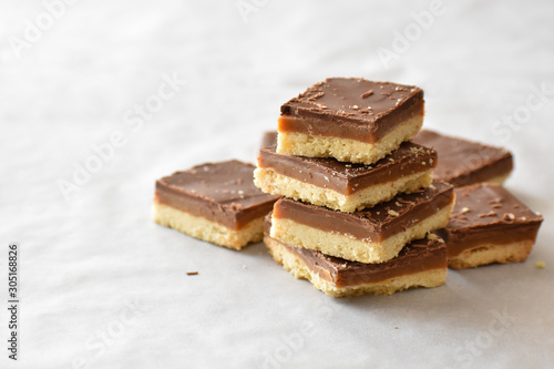 Millionaire's shortbread with chocolate and caramel on a parchment paper with copy space on the left side.