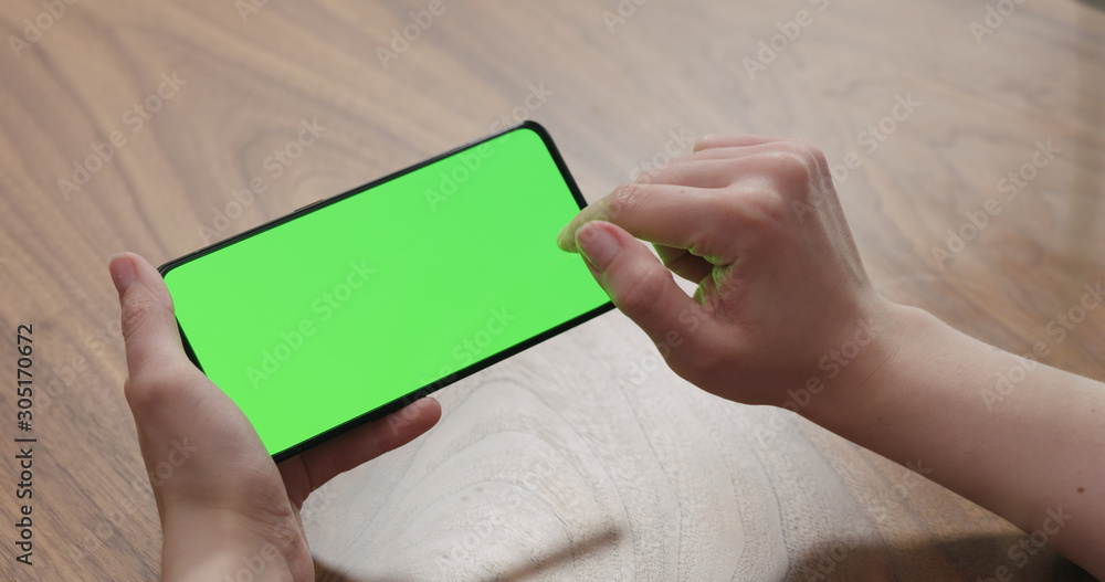 Young woman sitting at a table and using a smartphone with horizontal green screen Young woman sitting at a table and using a smartphone with horizontal green screen