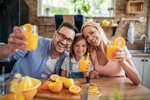 Foto Cheerful young family drinking orange juice