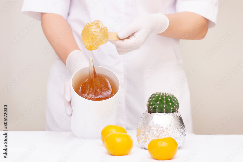 Shugaring master is holding a jar of shugaring paste in his hands. Nearby lies a cactus and tangerines. clean skin concept. light background. Shugaring master is holding a jar of shugaring paste in his hands. Nearby lies a cactus and tangerines. clean skin concept. light background.