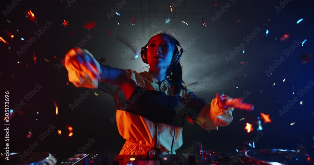 Professional female asian dj working in a nightclub, composing a mix, turning knobs and slider on her mixer controller, performing live in red and blue lights - nightlife concept 4k footage