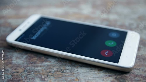 Incoming call on white mobile phone on wooden surface