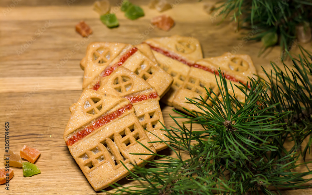 Christmas gingerbread cookies in the form of house on a wooden table surrounded by pine branches and colored candied fruits, flat lay Christmas gingerbread cookies in the form of house on a wooden table surrounded by pine branches and colored candied fruits, flat lay