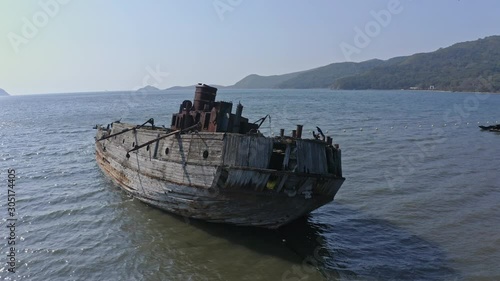 Ships graveyard. Slow pivot around the stern of a derelict partially submerged shipwreck, inclined on its starboard side, aground near the shore, with a bird landing  on its stern. photo