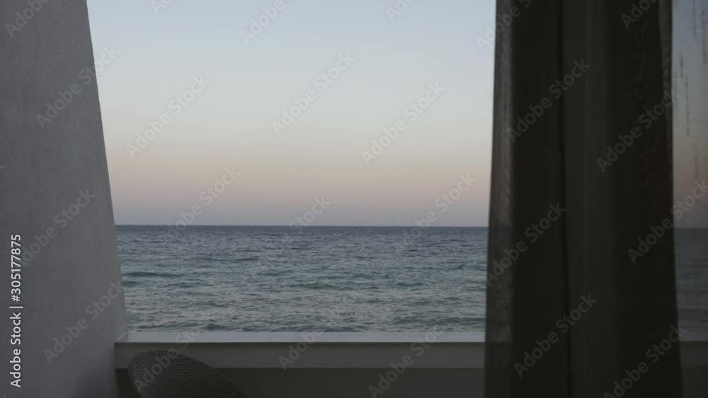View through the curtain from the hotel room through the balcony to the sea before sunset. View through the curtain from the hotel room through the balcony to the sea before sunset.