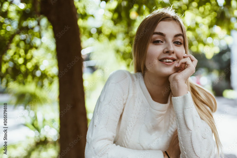 girl in a white sweater smiles affectionately propping her cheek with her hand in the background wood girl in a white sweater smiles affectionately propping her cheek with her hand in the background wood