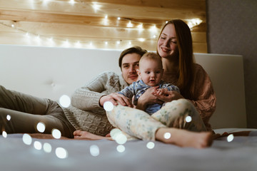 young family with a toddler. sitting on the floor of the room, smiling gently, lanterns sparkling all around, family idyll