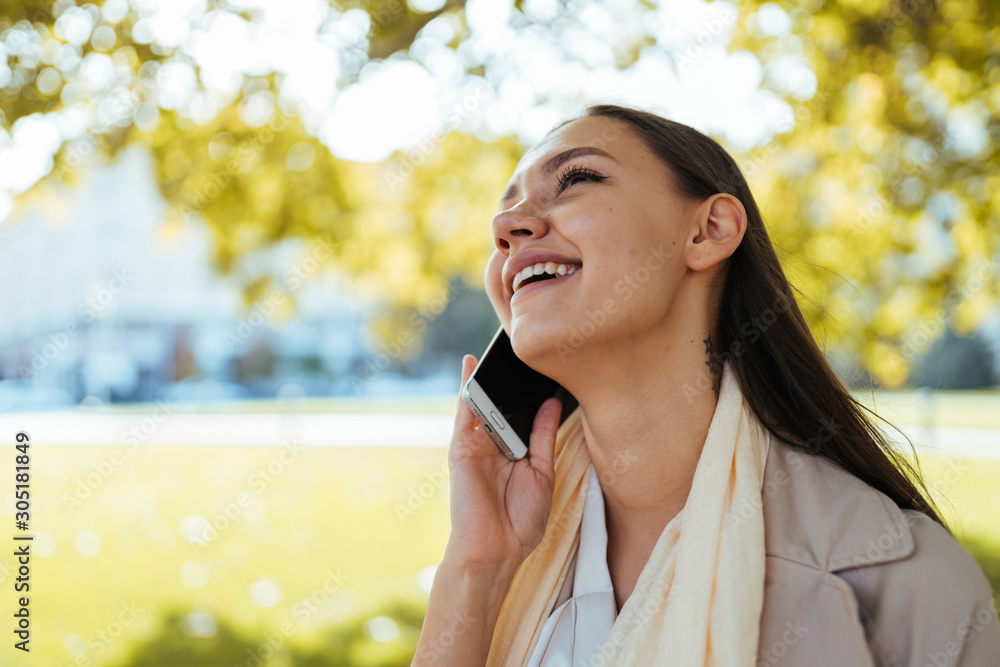 sunny autumn day, girl joyfully smiling, head slightly tilted up, talking on the phone sunny autumn day, girl joyfully smiling, head slightly tilted up, talking on the phone