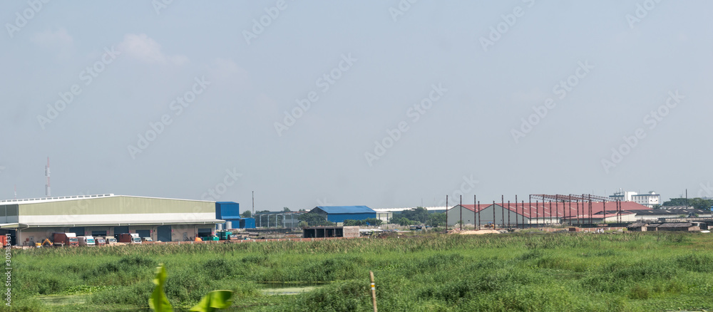 Industrial site power plant landscape. Industry surrounded by rural agricultural field and green summer meadow. A beautiful non-urban scenic environment of Rural Countryside of India, south asia pac.