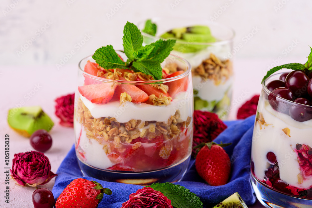healthy dessert with cherries, strawberries, kiwi, cream cheese ricotta, granola, mint in glass on blue napkin on light pink background healthy dessert with cherries, strawberries, kiwi, cream cheese ricotta, granola, mint in glass on blue napkin on light pink background