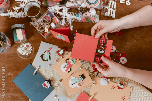 View of hands of young woman on table making handmade Christmas cards with Snowman and Santa