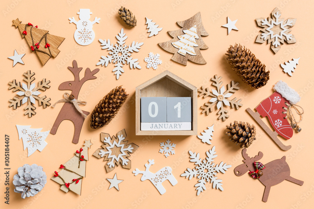 Top view of wooden calendar surrounded with New Year toys and decorations on orange background. The first of January. Christmas time concept Top view of wooden calendar surrounded with New Year toys and decorations on orange background. The first of January. Christmas time concept