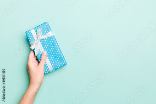 Woman hands give wrapped christmas or other holiday handmade present in colored paper. Present box, decoration of gift on Blue table, top view with copy space
