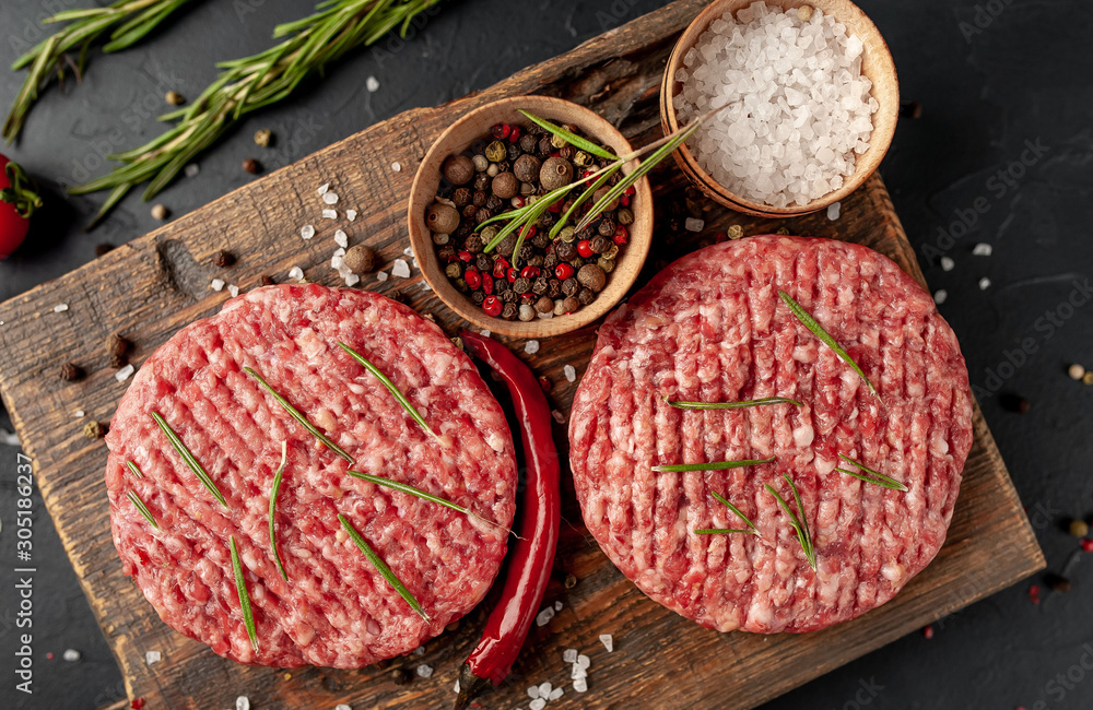 Raw beef burger cutlets with herbs and spices on a concrete background Raw beef burger cutlets with herbs and spices on a concrete background