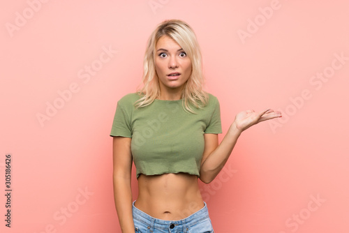 Young blonde woman over isolated pink background making doubts gesture © luismolinero