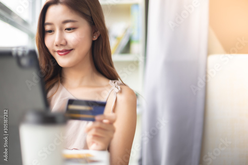 Happy Asian young woman doing online shopping at home.She holding credit card and using laptop computer.Smiling asian woman on couch using tablet to shop online n the living room.