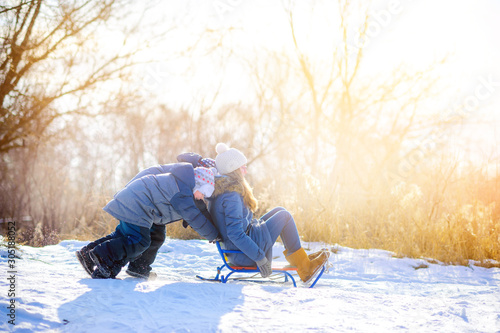 Happy children play in a snowy winter park at sunset. Sledding and having fun. Winter fun. Holidays.