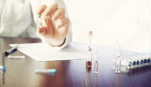 A man signs a medical document. Medical equipment on the table. Stethoscope and ampoules with syringes. Makes notes in the office. Medical center.