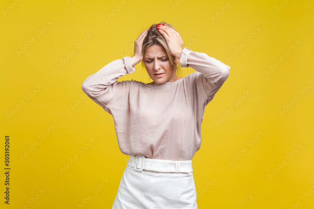 Portrait of depressed sick young woman with fair hair in casual blouse standing with closed eyes, holding head suffering migraine, mental disorder. indoor studio shot isolated on yellow background Portrait of depressed sick young woman with fair hair in casual blouse standing with closed eyes, holding head suffering migraine, mental disorder. indoor studio shot isolated on yellow background
