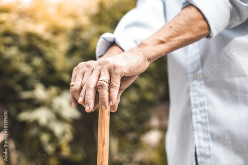 Close up of elderly hands in wrinkles holding walking stick.elderly old man with walking stick stand on footpath sidewalk crossing. © anon