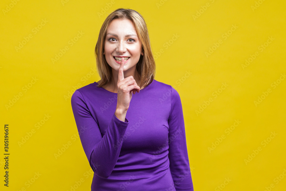 Don't say anyone! Portrait of cheerful woman in tight purple dress making silence quiet gesture with finger on her mouth, asking to keep secret gossip. indoor studio shot isolated on yellow background Don't say anyone! Portrait of cheerful woman in tight purple dress making silence quiet gesture with finger on her mouth, asking to keep secret gossip. indoor studio shot isolated on yellow background