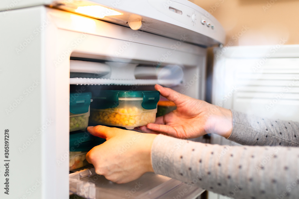Woman taking containers with frozen peas and corn out from freezer. Woman taking containers with frozen peas and corn out from freezer.