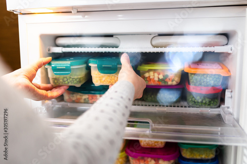 Woman taking containers with frozen peas and corn out from freezer. photo