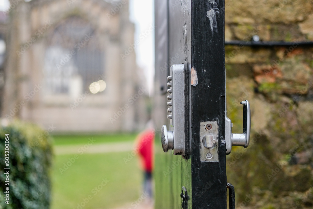 Shallow focus of a combination key pad on an open door leading to a famous, English cathedral. A man can be seen walking along a patch to the building. Shallow focus of a combination key pad on an open door leading to a famous, English cathedral. A man can be seen walking along a patch to the building.