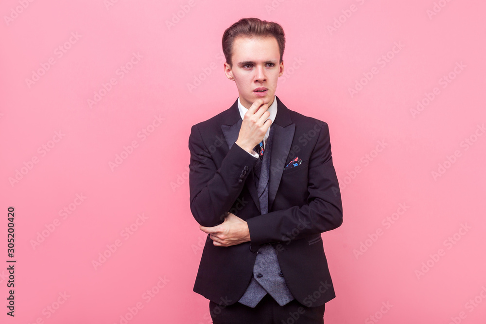 Let me think. Portrait of thoughtful smart man in expensive suit and with stylish haircut touching his chin and looking aside with puzzled face, pondering business plan. studio shot, pink background Let me think. Portrait of thoughtful smart man in expensive suit and with stylish haircut touching his chin and looking aside with puzzled face, pondering business plan. studio shot, pink background