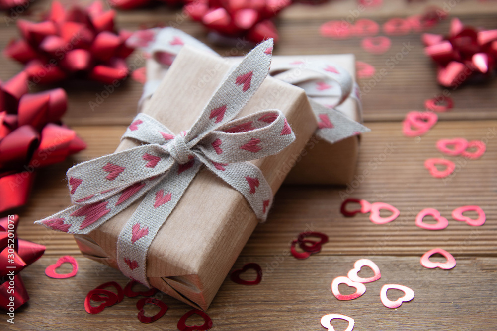Kraft brown paper gift box with red bows and confetti, on wooden background. Valentine's Day, Birthday, Party concept. Kraft brown paper gift box with red bows and confetti, on wooden background. Valentine's Day, Birthday, Party concept.