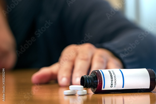 Prescription bottle with Oxycodone tablets on a table over a man wih blur hand. photo