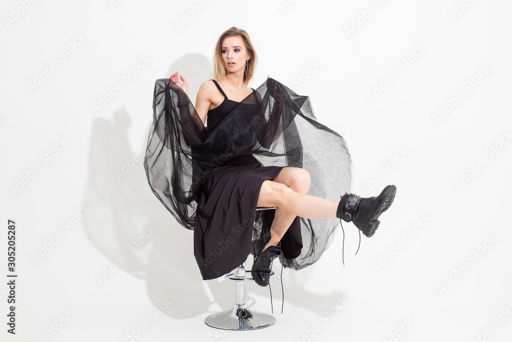 Fototapeta premium A girl in a t-shirt and a black skirt sits on a chair on a white background. Fashion shooting