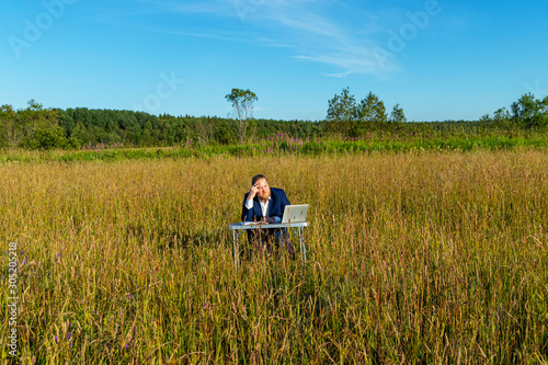 White caucasian man with a beard works at table on a laptop outdoors. Concept businessman outdoors.