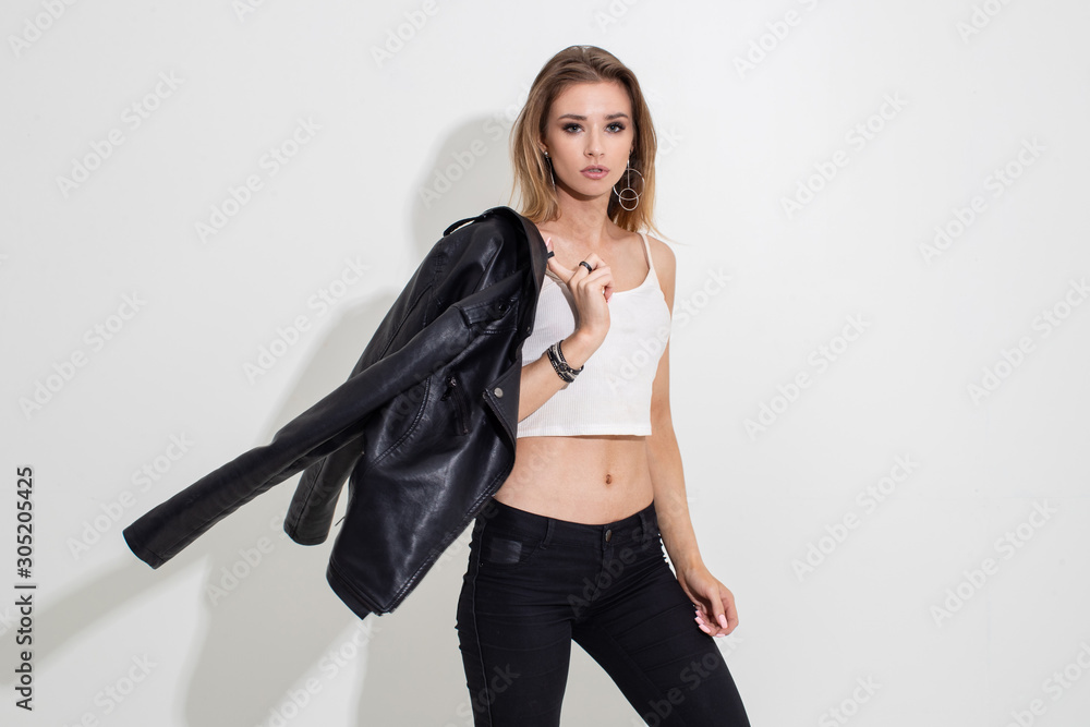 A girl in a leather jacket and black pants posing on a white background. Fashion shooting - obrazy, fototapety, plakaty 