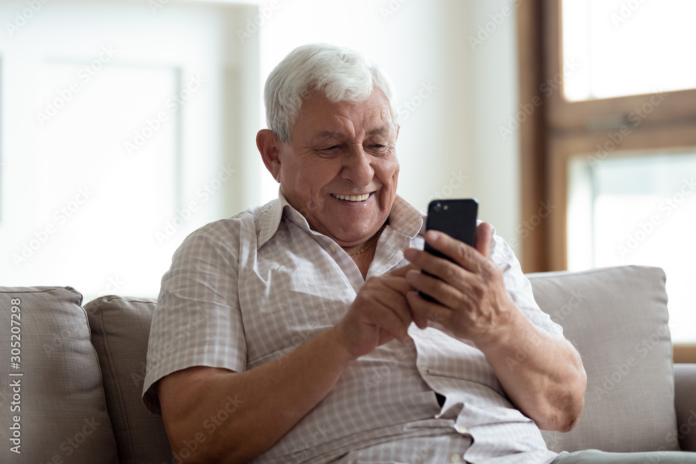 Happy older man sitting on sofa at home, using smartphone. Happy older man sitting on sofa at home, using smartphone.