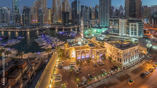 Yachts in Dubai Marina flanked by the Al Rahim Mosque and residential towers and skyscrapers aerial night to day timelapse.