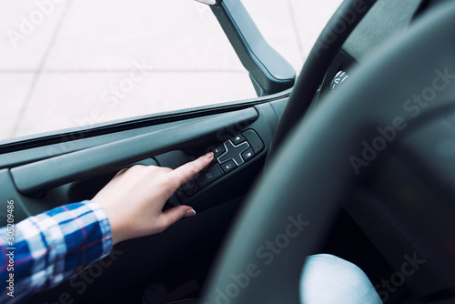 Driver's hands pressing button to roll window up in vehicle.