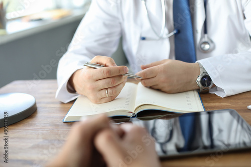 Doctor listening to the patient while he is telling about his problems. Male doctor taking notes. Just hands over the table.