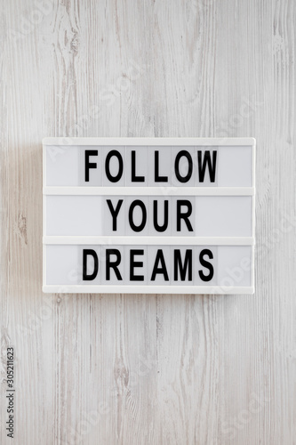 'Follow your dreams' words on a modern board on a white wooden background, top view. Overhead, from above, flat lay.