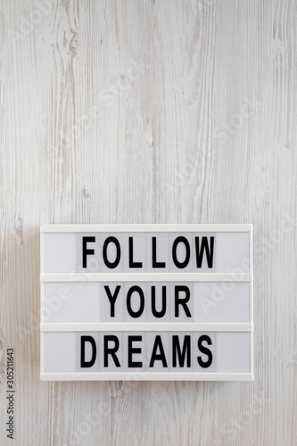 'Follow your dreams' words on a lightbox on a white wooden background, top view. Overhead, from above, flat lay. Copy space.