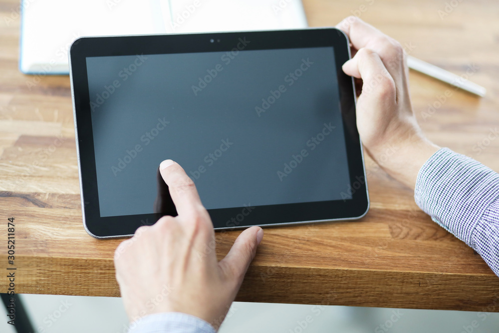 Man's hands holding blank tablet device over a wooden workspace table. Man's hands holding blank tablet device over a wooden workspace table.