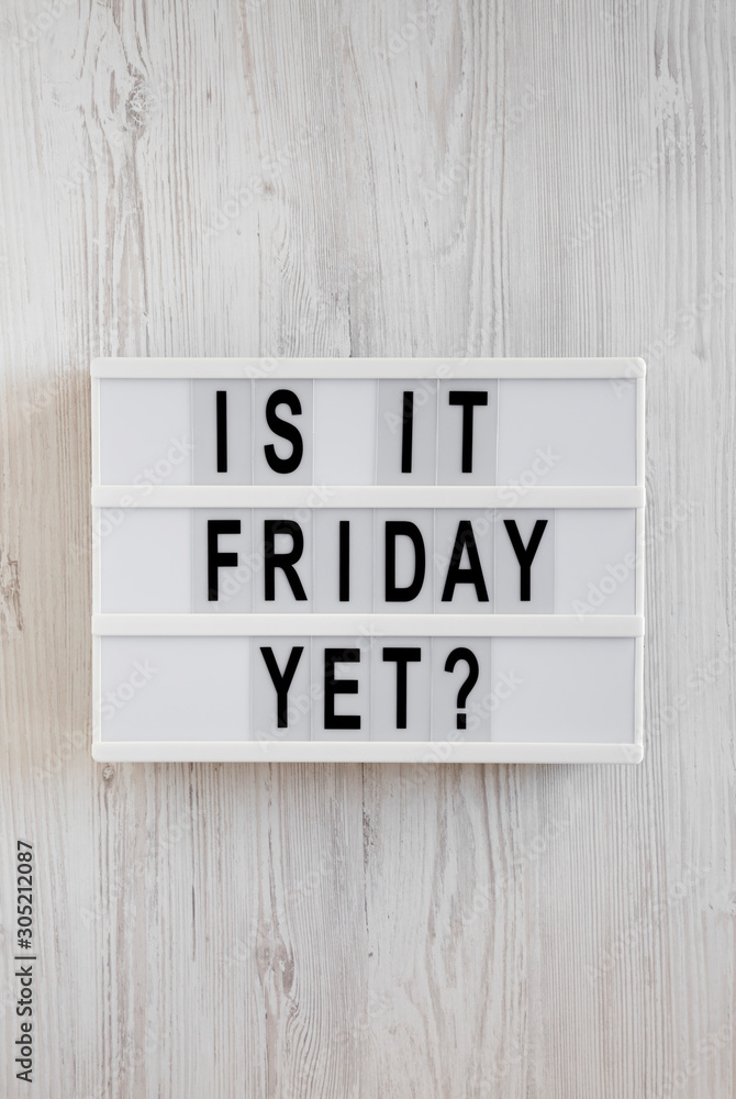 'Is it friday yet?' words on a modern board on a white wooden background, top view. Overhead, from above, flat lay. Close-up.