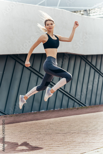 Young woman with fit body jumping and running against grey background.