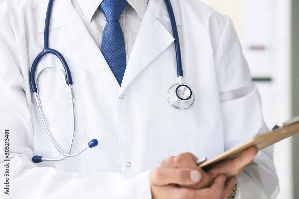 Close-up of clipboard with blank paper in medical doctor hand. Male doctor listens to the patient holding a clipboard with documents for hospitalization. Close-up of clipboard with blank paper in medical doctor hand. Male doctor listens to the patient holding a clipboard with documents for hospitalization.