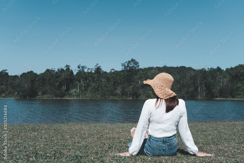 Young women wearing white shirts, hats, are relaxing, happy, sitting on the grass and looking away rivers, mountains. Travel nature and outdoor concepts