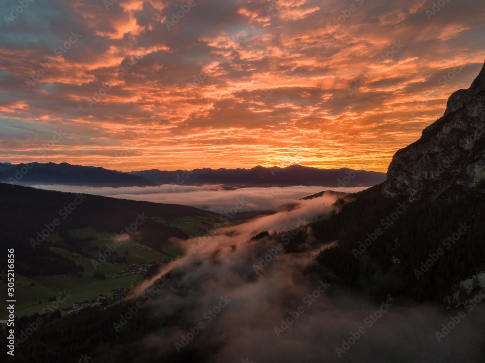 Aerial view of the sunrise from the mountain in Dolomites, Italy. Drone view with morning glow and mist in the valley