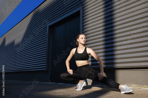 Young woman with fit body jumping and running against grey background. Female model in sportswear exercising outdoors