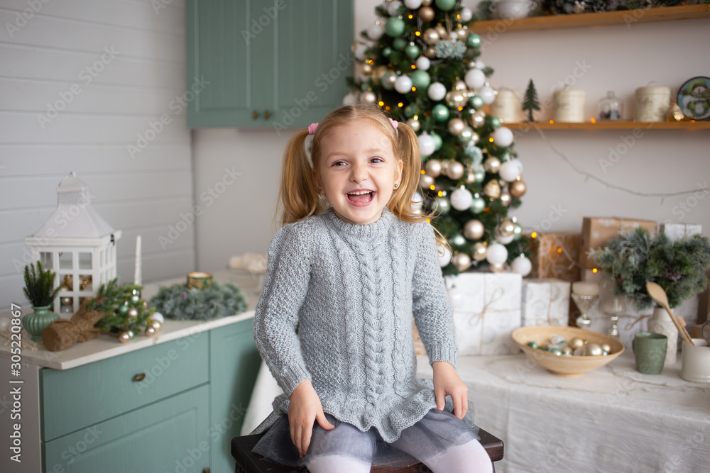 laughing girl is sitting in kitchen near decorated Christmas tree indoors. laughing girl is sitting in kitchen near decorated Christmas tree indoors.