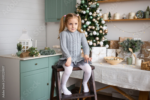 Merry Christmas and Happy Holidays. Cute little child girl is sitting near decorated Christmas tree indoors.
